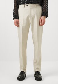 Beige skräddarsydda byxor med en slät textur, med platt front, sidofickor och en enkel knappstängning. Matchas med svarta skor.