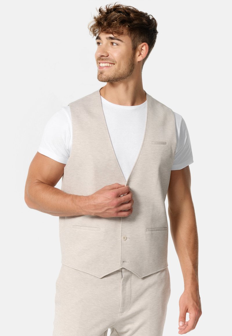 Chaleco gris claro hecho de una tela suave, con un diseño de cuello en V, dos bolsillos en la parte delantera y un cierre con botones en el frente.