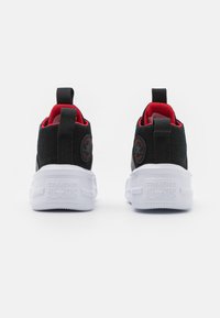 Czarne i czerwone niskie trampki Converse All Star pokazane od tyłu, z białymi grubymi podeszwami i pętelkami na piętach.