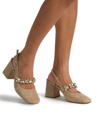 Zapatos de tacón cuadrado de ante beige, con puntera cuadrada, que cuentan con una correa decorativa embellecida con gemas transparentes y un diseño ajustable de tira detrás.