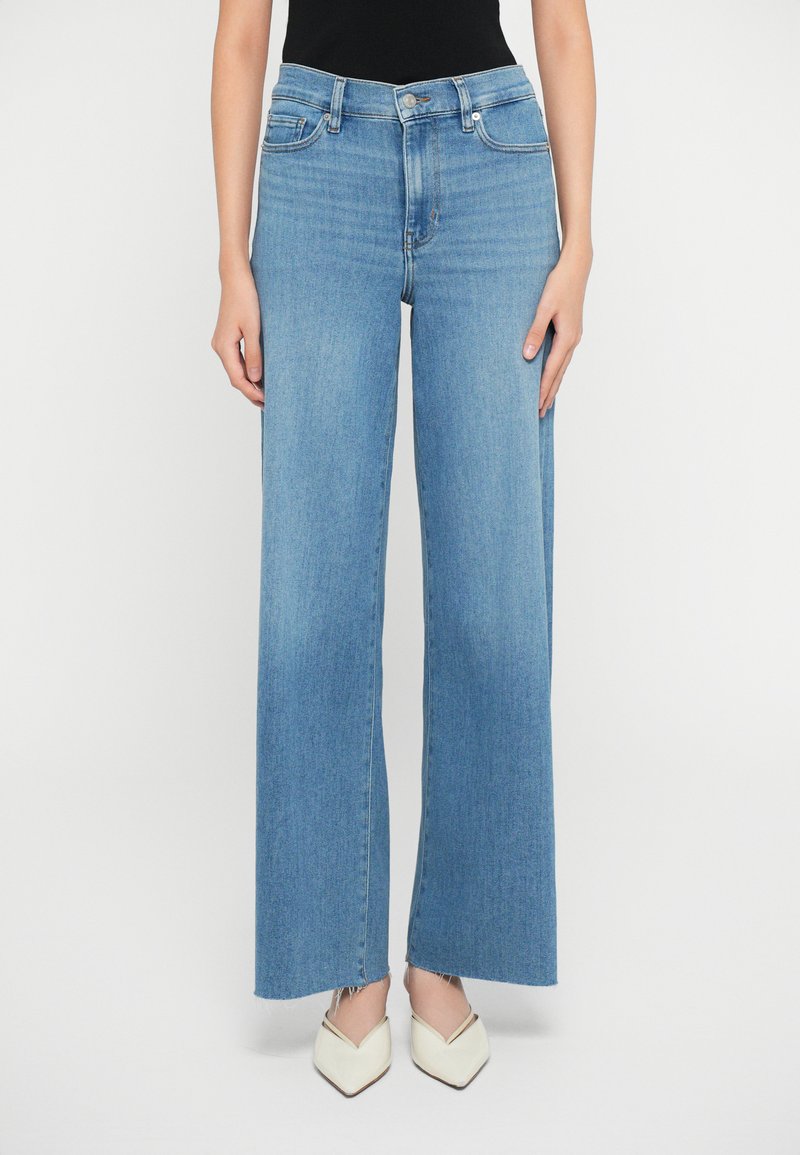 Lyseblå vide jeans lavet af denim, med høj talje, frynset kant og sidelommer. Sat sammen med hvide spidse sko.
