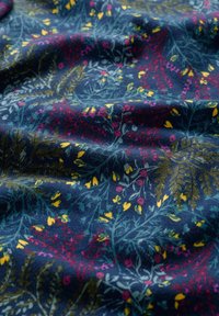 Tejido azul marino con un patrón floral que presenta hojas verdes, flores amarillas, rosas y rojas. Textura suave con un ligero brillo.