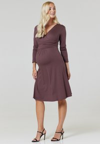 Maternity dress in dark mauve, featuring a V-neck, long sleeves, and gathered detailing at the waist. Soft, stretchy fabric with a flowing skirt.