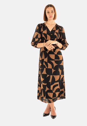 Robe à motifs noirs et bruns avec un décolleté en V, des manches ¾ et une silhouette fluide, associée à des chaussures à talons hauts noires.