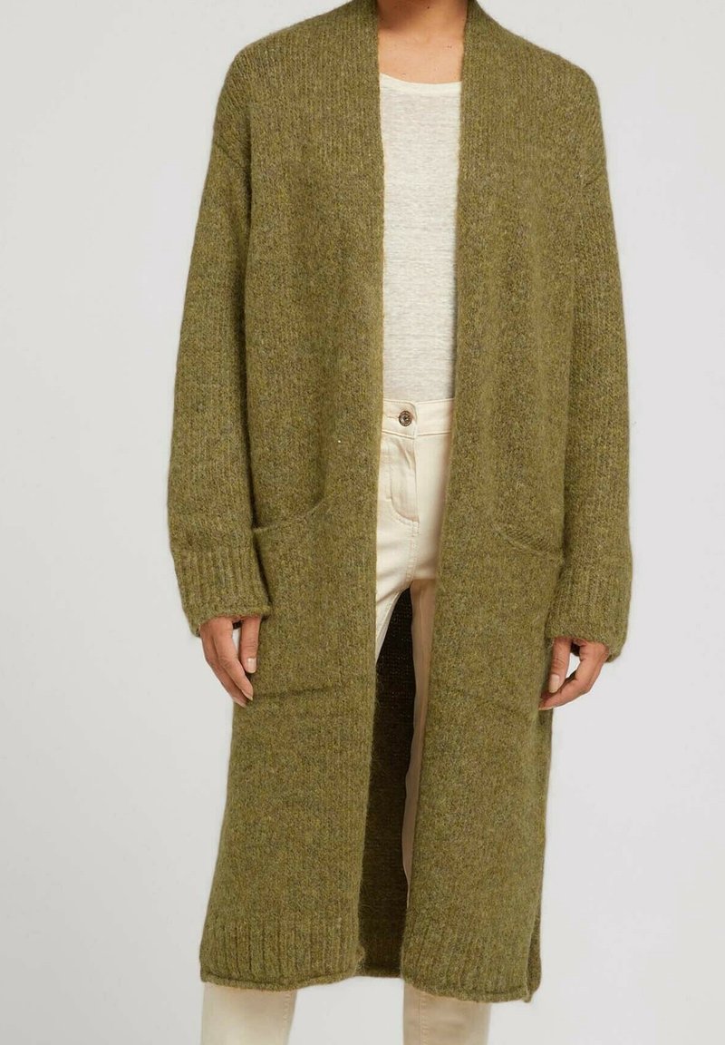 Longue carte cardigan vert olive en tricot avec poches avant, porté avec un pantalon beige et un haut gris clair.
