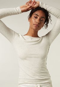 Top de manga larga en gris claro, confeccionado con una suave tela texturada, que presenta un escote redondeado y detalles en las costuras laterales.