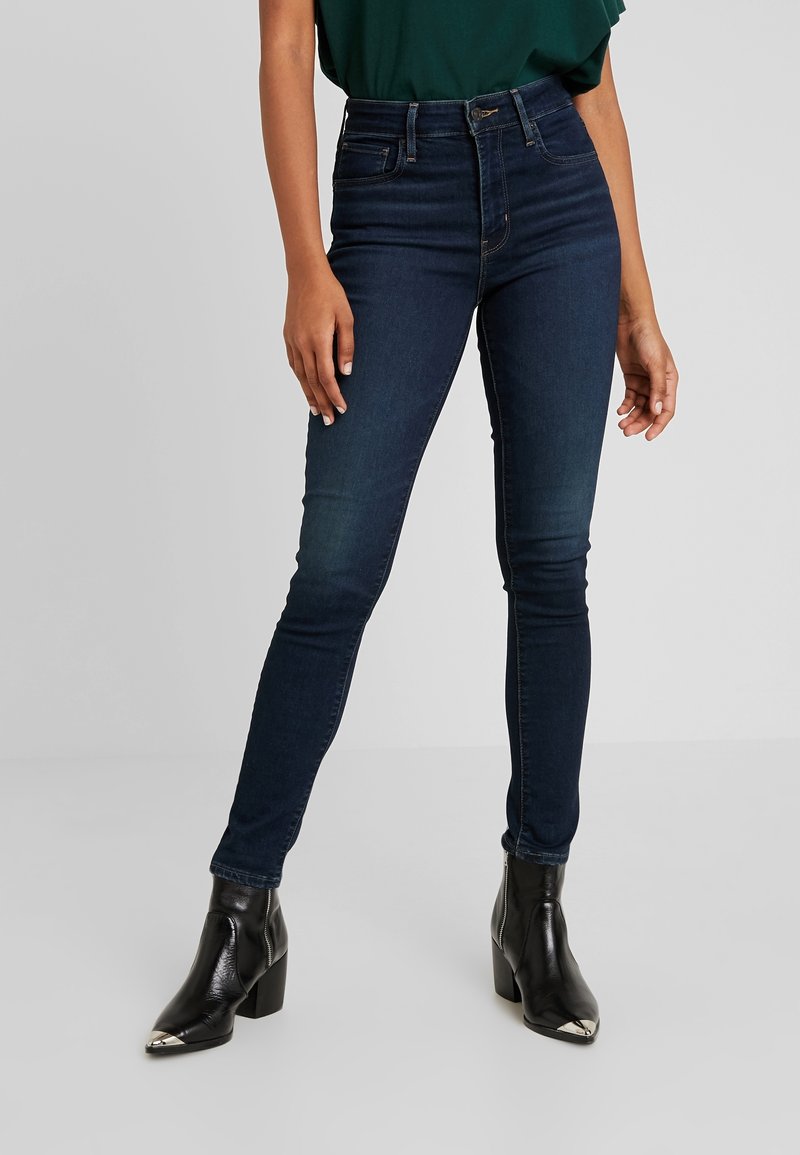 Mörkblå högmidjade skinny jeans i denim, med en klassisk design med fem fickor och en subtil blekning. Bärs med svarta ankelbotten.