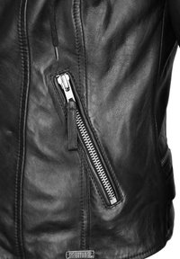 Schwarze Lederjacke mit einer sichtbaren Reißverschlusstasche, texturiertem Finish und Steppdetails; ausgestattet mit einem metallischen Reißverschluss mit Zuglasche.