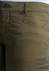 Olivově zelené kalhoty vyrobené z hladké tkaniny, s předním zapínáním na knoflík, poutky na pásek a malou štítkovou nášivkou poblíž pasu.