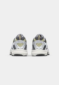 Chaussures de sport grises et blanches avec des accents jaunes, tige en maille, col rembourré et semelle texturée. Comprend un logo près du talon.
