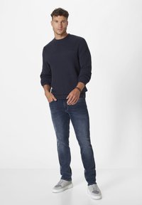 Navy gestrickter Rundhalspullover, strukturiert mit horizontalen Rippungen, kombiniert mit medium-waschengrauen Slim-Fit-Jeans und grauen Sneakern.