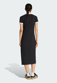 Czarna sukienka do kolan z białymi wykończeniami, krótkimi rękawami i luźnym krojem. Stylizowana z czarno-białymi sneakersami, z plecioną fryzurą.