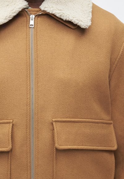 Καφέ ζακέτα με φερμουάρ και υφή εξωτερική, κρέμα φλις κολάρο και δύο μπροστινές τσέπες. Διακοσμημένη με γυαλιστερό μεταλλικό υλικό φερμουάρ.
