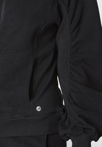 Felpa nera con zip, caratterizzata da dettagli arricciati sulle maniche, polsini a costine e un'etichetta con logo all'orlo. Realizzata in morbido cotone.