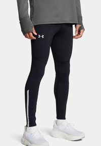Leggings sportivi neri con un design testurizzato, caratterizzati da una striscia laterale bianca e un logo Under Armour sulla parte inferiore della gamba. Abbinati a sneakers bianche.