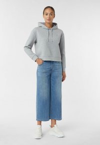 Grau geschnittene Kapuzenjacke mit Kordelzügen, kombiniert mit weit geschnittenen, hellblauen Jeans und weißen Sneakers. Minimalistisches Design, weiche Texturen.