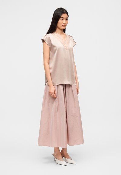 Επάνω μέρος από απαλό ροζ σατέν με κοντά μανίκια και δαντελωτή V-λαιμόκοψη, συνδυασμένο με ογκώδη φούστα στον ίδιο τόνο. Λευκά παπούτσια slip-on με διακοσμητικές λεπτομέρειες.