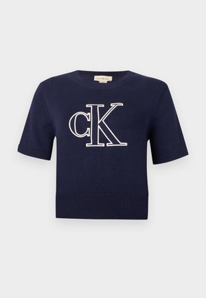 Camiseta de punto de color azul marino de manga corta con dobladillo y puños acanalados, que presenta el logo grande "cK" bordado en blanco centrado en el pecho.