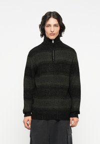 Strickpullover mit hohem Kragen und Reißverschluss. Er hat ein gestreiftes Muster in dunklen Grüntönen und Schwarz, mit einer strukturierten Oberfläche.