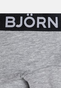Grå t-shirt med kort ärm som har ett svart midjeband med "BJÖRN" i vit text. Tyget har en mjuk, strukturerad yta.