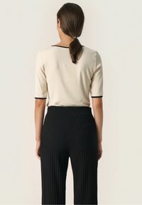 Cream short-sleeve top with black trim paired with black ribbed wide-leg trousers. The materials appear smooth and textured.