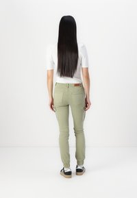 Groene cargobroek met aangesloten manchetten, zijvakken en een gestructureerde afwerking. Gekleed met een witte top en zwarte sneakers, gezien van achteren.