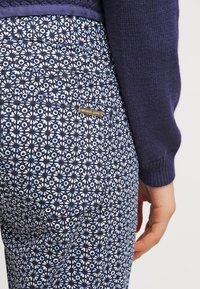 Pantalones navy con un patrón floral en azul claro y blanco. Presenta una pequeña etiqueta de logo dorado en el bolsillo trasero. Material de mezcla de algodón.
