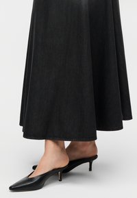 Μαύρη τζιν φούστα με ρέον σχέδιο, σε συνδυασμό με μαύρα δερμάτινα mules με μυτερή μύτη και λεπτό, κομψό τακούνι.