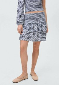Gonna mini azzurra a fantasia con orlo a più strati e volant. Realizzata in tessuto leggero, presenta una vita arricciata e un top coordinato. Scarpe piatte con lacci.