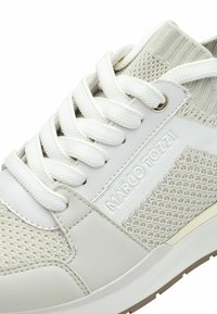 Sneaker bianco con una tomaia in tessuto a maglia, dettagli in pelle, lacci rotondi e logo sul lato; suola testurizzata.
