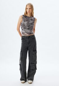 Top sin mangas de patrón negro y gris con tejido texturizado y diseño drapeado, combinado con pantalones cargo de pierna ancha que cuentan con múltiples bolsillos.