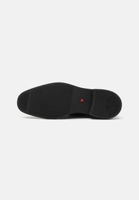 Semelle de chaussure noire avec une texture lisse, présentant un accent carré rouge central, une forme profilée et des motifs de grip diagonaux.