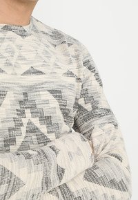 Maglione leggero a girocollo color crema con motivi geometrici grigi; lavorazione a maglia strutturata, maniche lunghe e vestibilità rilassata.