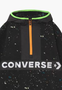 Czarny polar z żywym pomarańczowym suwakiem do połowy, z czarną wstawką i białym logo "CONVERSE" na klatce piersiowej oraz zielonym wykończeniem kaptura.