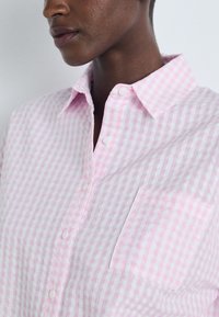 Ροζ και λευκή καρό πουκάμισο με κουμπωτό γιακά, μπροστινή τσέπη και υφή υφάσματος.