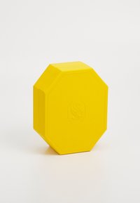 Cutie octogonal galbenă cu o suprafață texturată și un logo embosat. Dispune de un capac plat și margini netede. Designul este minimalist și geometric.