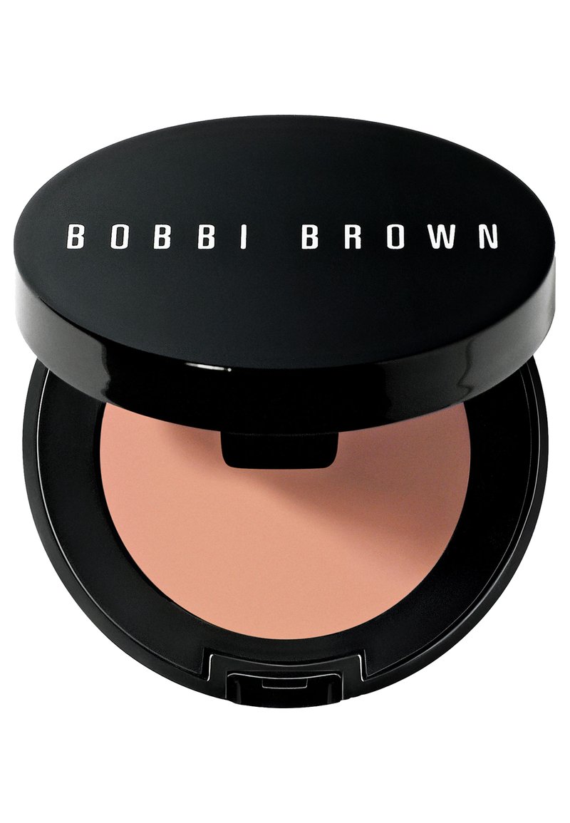 Svart kompakt sminkfodral med en slät yta, som har texten "BOBBI BROWN" i vitt. Inuti finns en rund persikofärgad puderpanna.