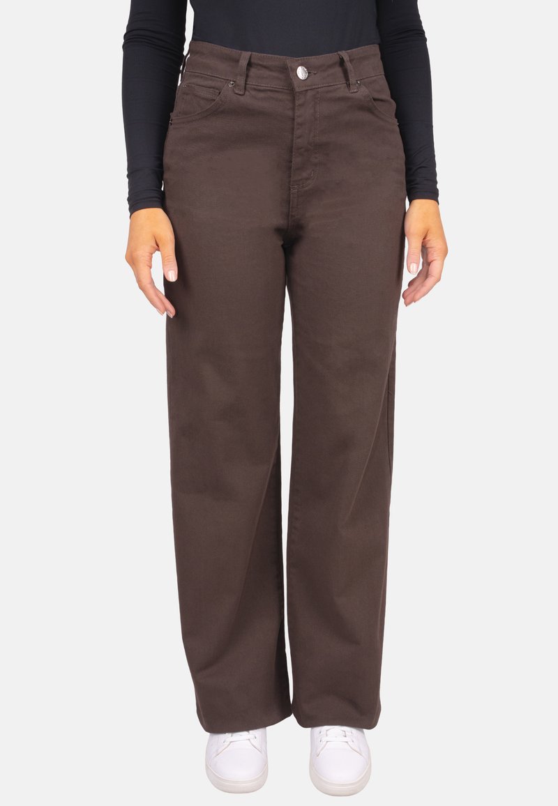 Pantalon large marron en coton, avec poches avant, fermeture par bouton, et texture lisse, porté avec un haut noir à manches longues.