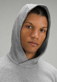 Szara, teksturowana bluza z kapturem o wysokim kołnierzu, z widocznymi szwami i miękkim, tkanym wyglądem. Minimalistyczny design.