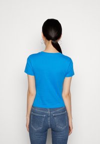 Camiseta corta de algodón azul con cuello redondo, mangas cortas y un corte ligeramente cropped, combinada con jeans ajustados azules.