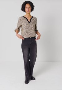 Bluse mit Leopardenmuster in Tan und Schwarz, V-Ausschnitt und schwarzem Saum, kombiniert mit hochtaillierten schwarzen Jeans und schwarzen Schuhen.