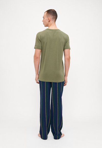 T-shirt vert olive à manches courtes, associé à un pantalon rayé bleu marine avec des lignes vertes et jaunes. Tissu lisse, coupe décontractée.