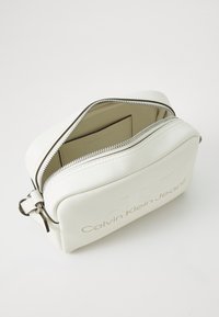 Borsa a tracolla in ecopelle bianca con chiusura a zip; presenta il logo "Calvin Klein Jeans" in rilievo sul davanti.