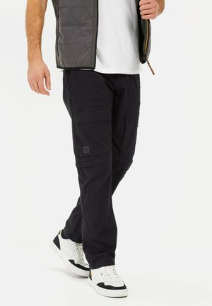 Black cargo pants made of durable fabric with multiple pockets. Paired with a white shirt and gray quilted vest, complemented by white sneakers.