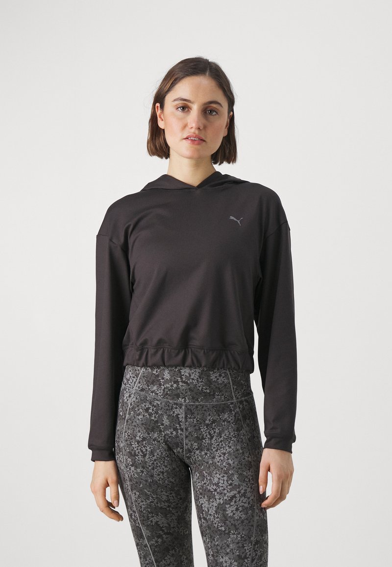 Felpa nera corta con maniche lunghe e cappuccio con cordino, con un piccolo logo Puma. Abbinata a leggings scuri con motivo floreale.