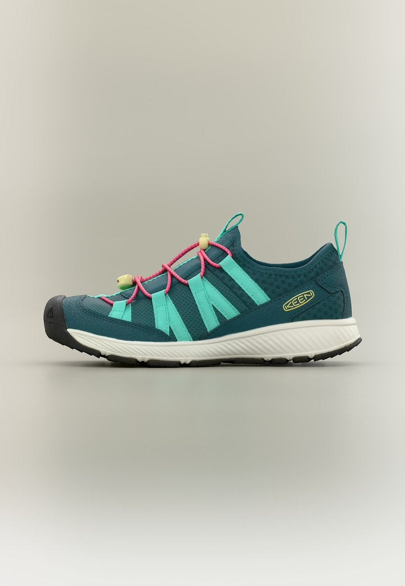 Chaussure sportive décontractée turquoise avec lacets élastiques roses, sangles turquoises, semelle noire et logo de marque jaune sur le côté.