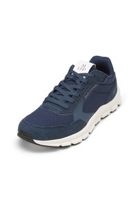 Baskets de sport bleu marine mettant en avant un mélange de matériaux en mesh et en suède, avec des lacets prononcés, un col rembourré et un logo blanc sur la languette.