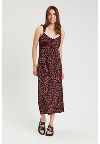 Robe midi fleurie avec un fond noir, ornée de fleurs roses, à fines bretelles et un corsage ajusté. Associée à des sandales noires à boucle.