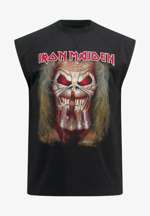 T-shirt sans manches noir avec un graphique d'un crâne aux yeux rouges et aux longs cheveux, affichant un geste de main. Texte "Iron Maiden" au-dessus.
