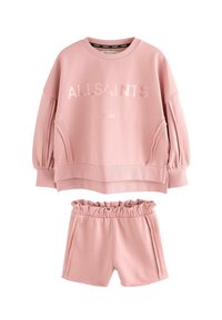 Rausvos medvilnės laisvalaikio komplektas, kuriame yra crewneck tipo sweatshirt su įspaustu tekstu ir laisvomis šortais su banguota juosmens linija.